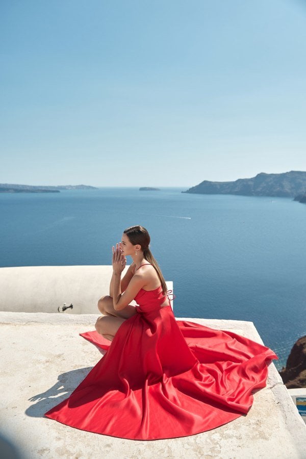 Κόκκινο σατέν βραδινό φόρεμα με ανοιχτή πλάτη, πλάγια όψη σε καθιστή στάση.